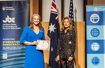 Dr Madison Paton holding a certificate and smiling to camera during the ceremony where she received a Fullbright Fellowship at Duke University to advance access to cord blood treatment for CP.