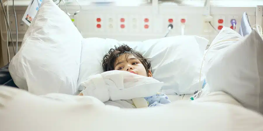 A young boy lying in a hospital bed with bandages on his arm