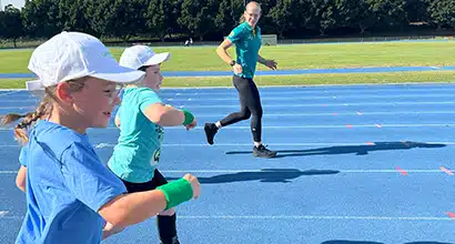 Two young children running on an athletics track with a therapist running alongside them