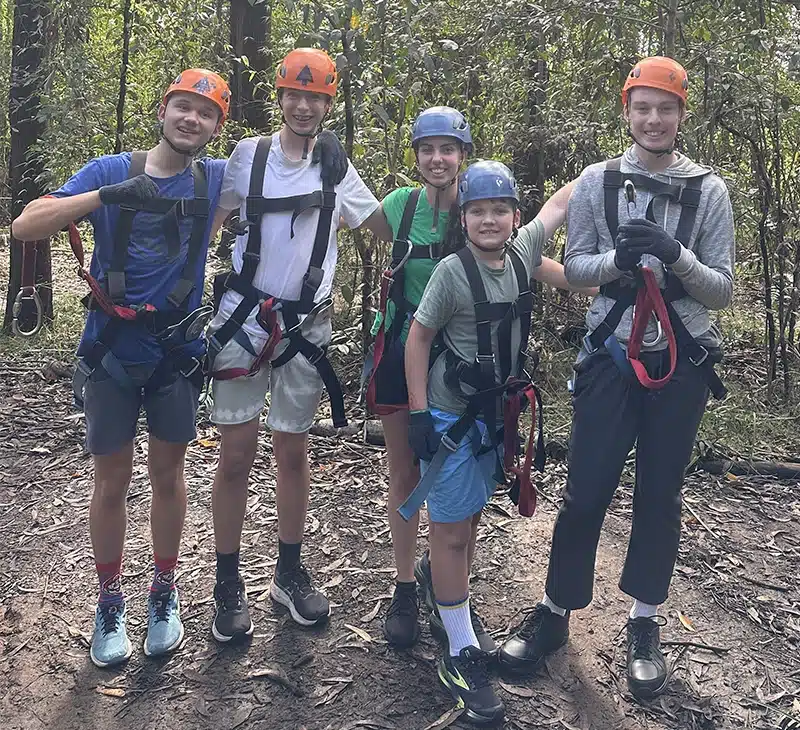 A group of kids wearing harnesses and helmets ready to climb at treetops on the central coast