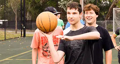 A teenage boy holds a basketball ready to shoot, while a line of boys forms behind him waiting for their turn