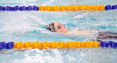 View from the side of the pool while a young boy swims backstroke in a middle lane