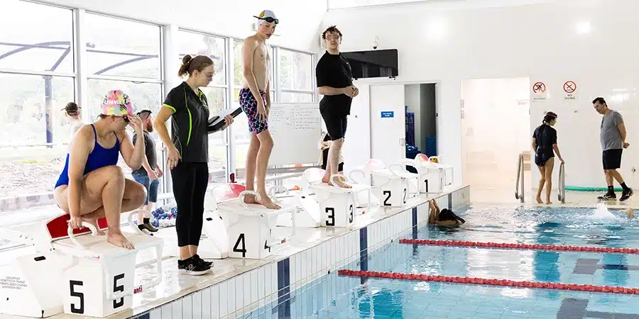 Participants of the camp lined up on diving blocks ready to swim at the swim-tri camp.