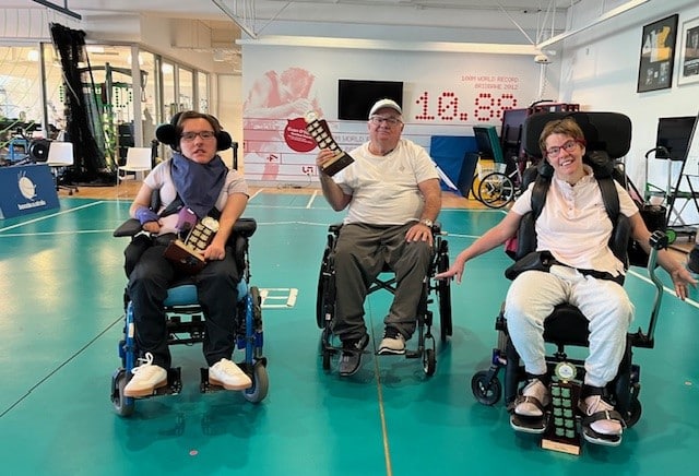 Three Wheelchair Boccia players lined up for a photo with their trophies