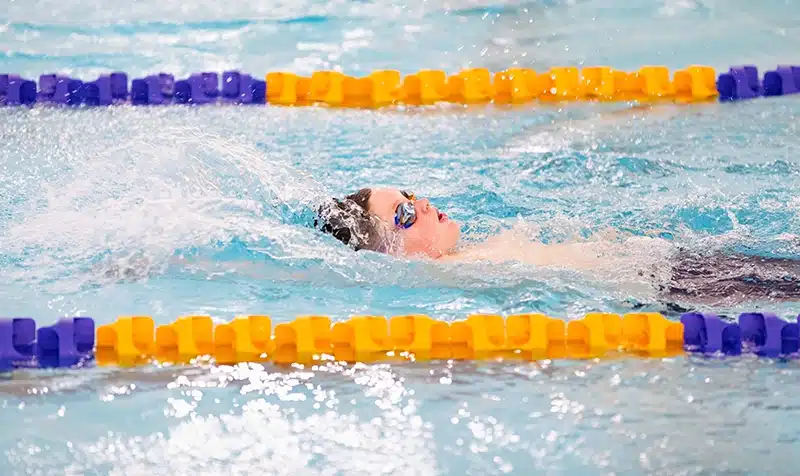 View from the side of the pool while a young boy swims backstroke in a middle lane