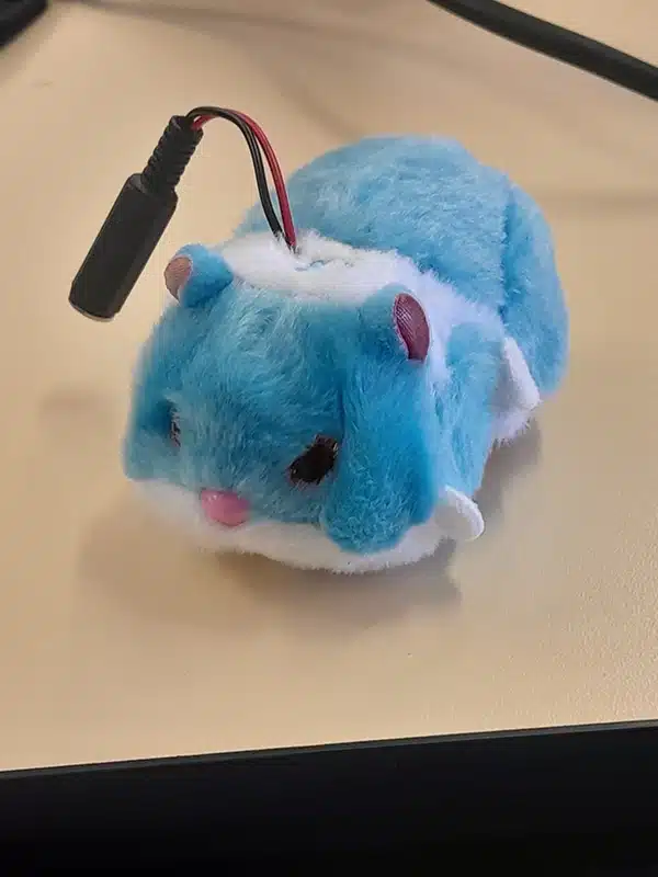 A small blue and white mouse toy with a cord coming out of it after being modified at the switch adapt workshop