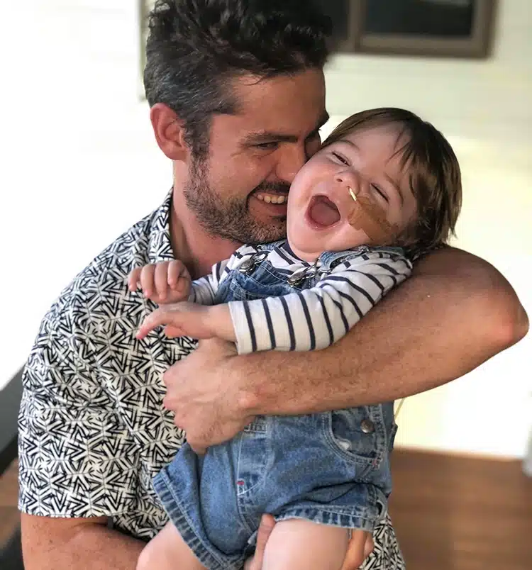A dad holding and cuddling his smiling baby boy who has a medical tube taped onto his face
