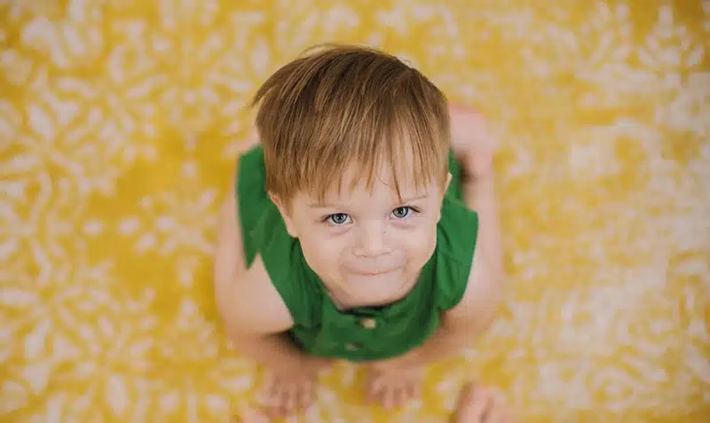 A baby sitting on the floor looking up to a camera