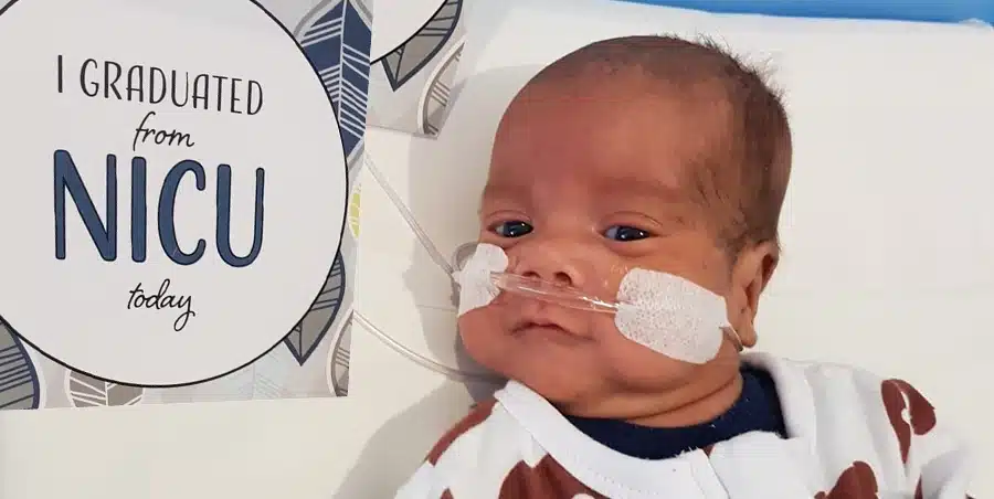 A baby in on a bed in NICU next to a sign that says i graduated NICU today
