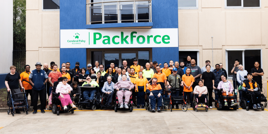 A group of supported employment workers and their disability support coordinators smiling for a photo in front of packforce