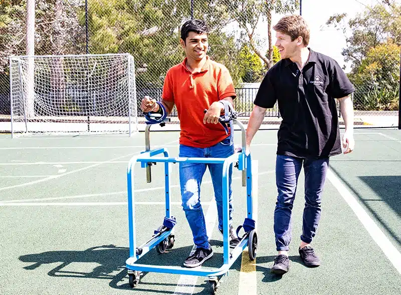A young adult male with cerebral palsy smiling during a functional capacity assessment outside on a sports court with an occupational therapist