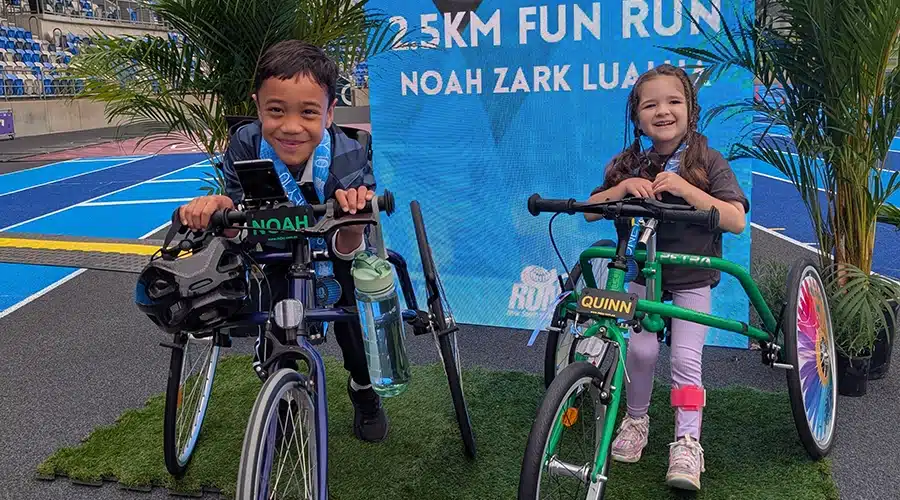 Noah and Quinn posing in their frame runners in front of the race banner