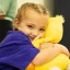 Young girl Mackenzie cuddling a soft yellow toy and smiling to camera