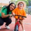 A young boy on a balance bike smiling to camera with a woman crouched down beside him also smiling to camera