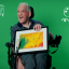 White elderly man holding painting sitting in a wheelchair laughing
