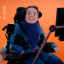 White woman with short dark hair in wheelchair on orange background