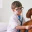 A little boy dressed up as a doctor holds a stethoscope to a large teddy bears chest