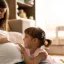 Pregnant mother sitting with her little girl, both touching her stomach and smiling at each other