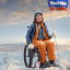 Eva Kalpidis sitting in her wheelchair on top of a snowy mountain peak holding a weet-bix flag